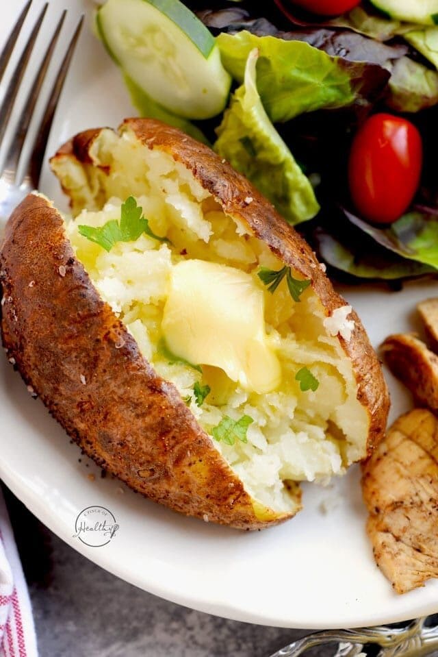 Homemade Air Fryer Baked Potato garnished with butter and parsley with fresh lettuce, cucumber and tomatoes on the side