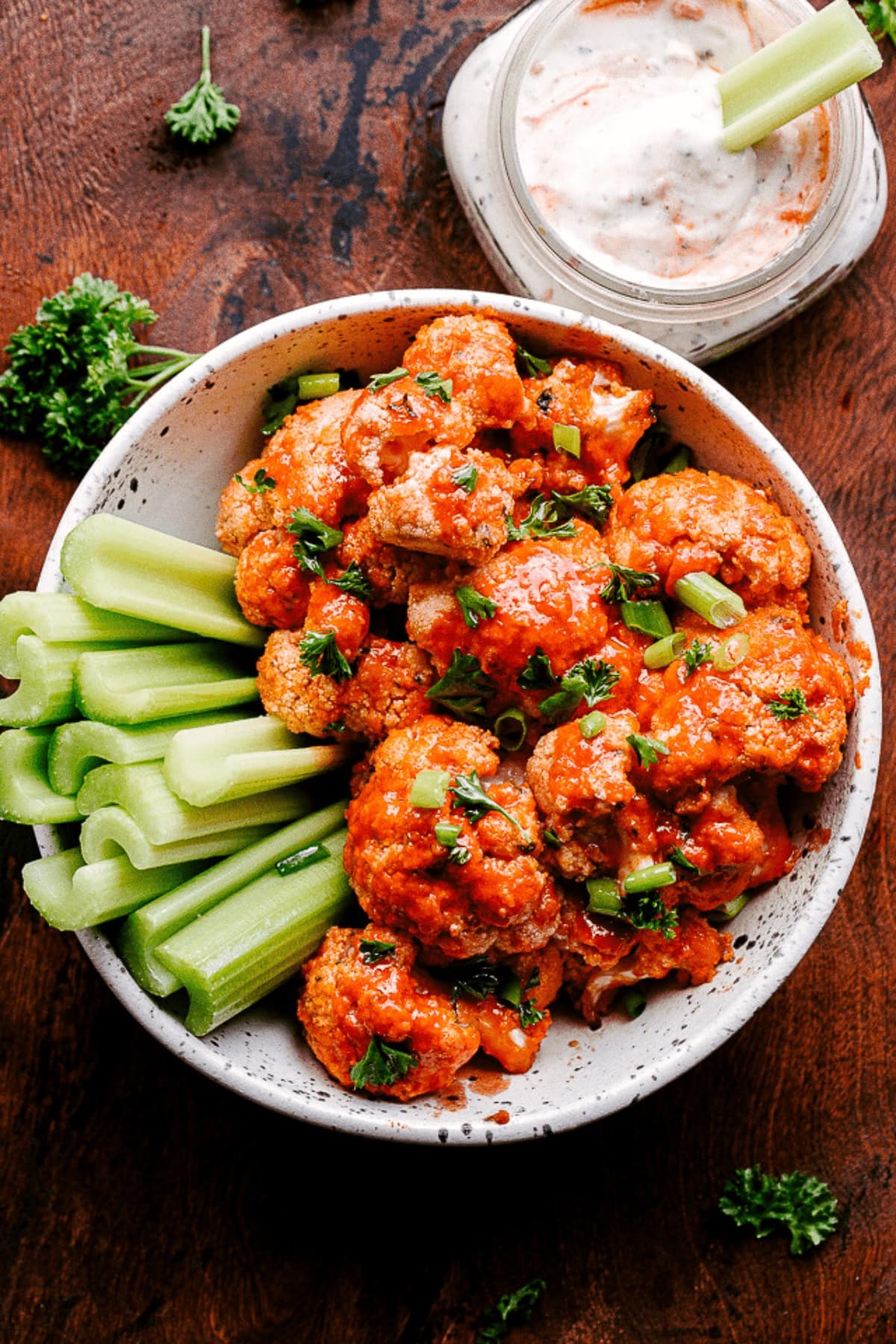 Bowl of homemade Air Fryer Buffalo Cauliflower Bites with celery stalks on the side garnish with parsley