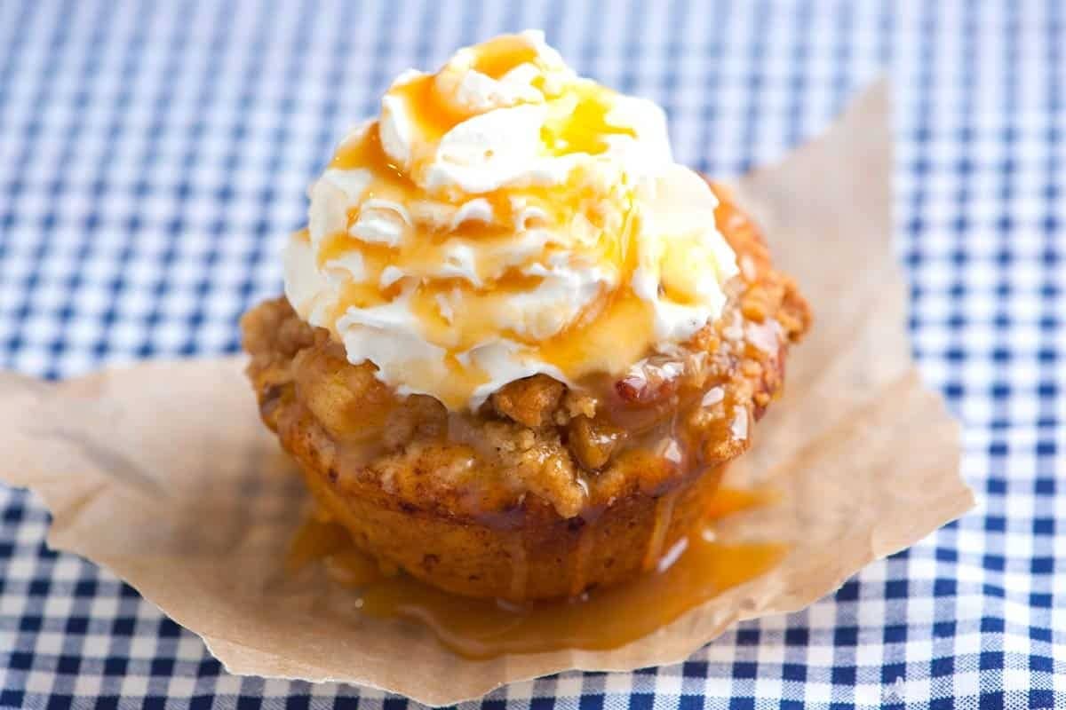 Apple pie cupcakes with whipped cream on top drizzled with caramel syrup.