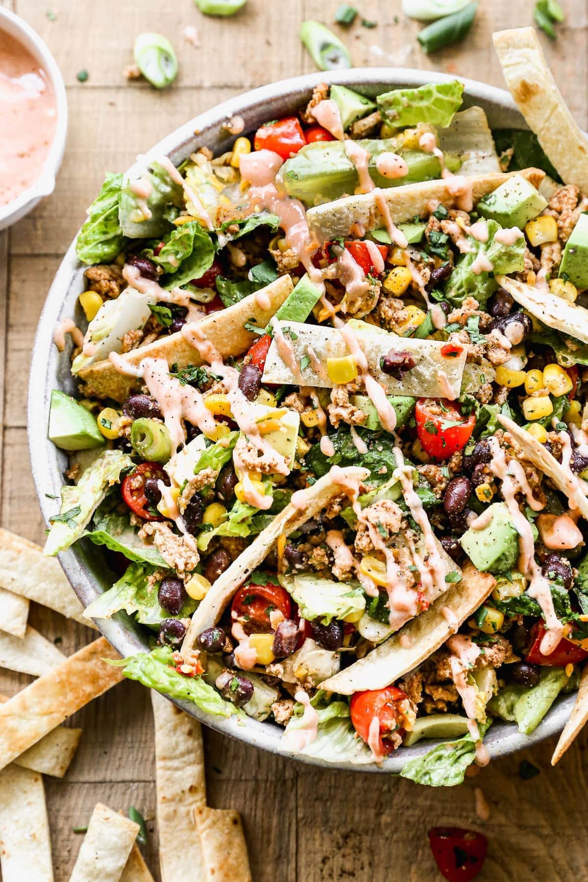 Taco salad with corn, tomatoes, avocados, lettuce, beans and baked tortillas, drizzled with dressing.
