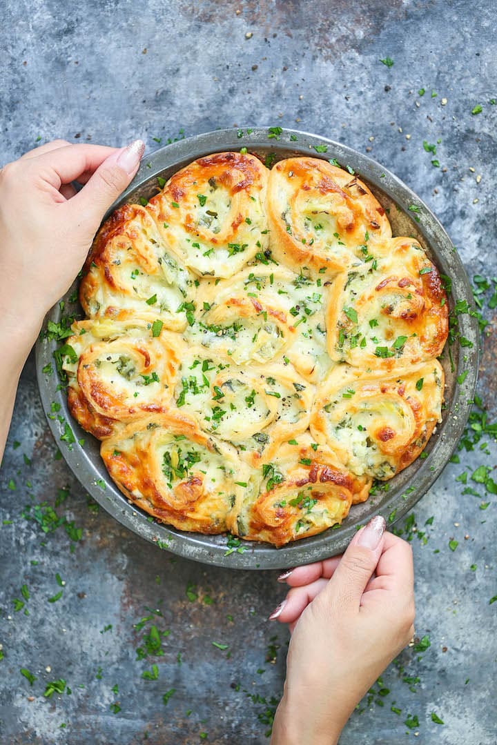 A Woman's Hand Holding a Pan of Spinach and Artichoke Pinwheels Ready to Serve