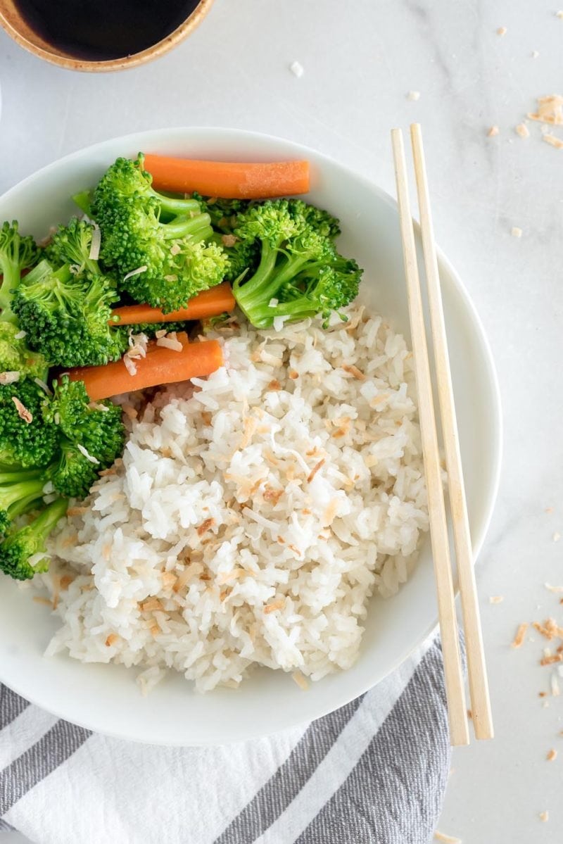 Coconut rice served with blanched broccoli and carrots with chopsticks.