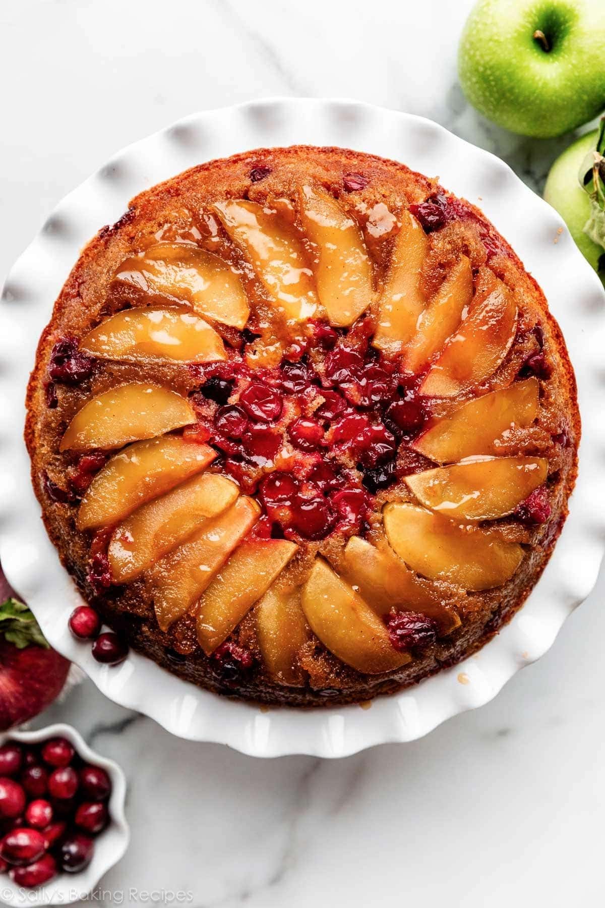 Upside down cake topped with slices of apples and cranberries with syrup.