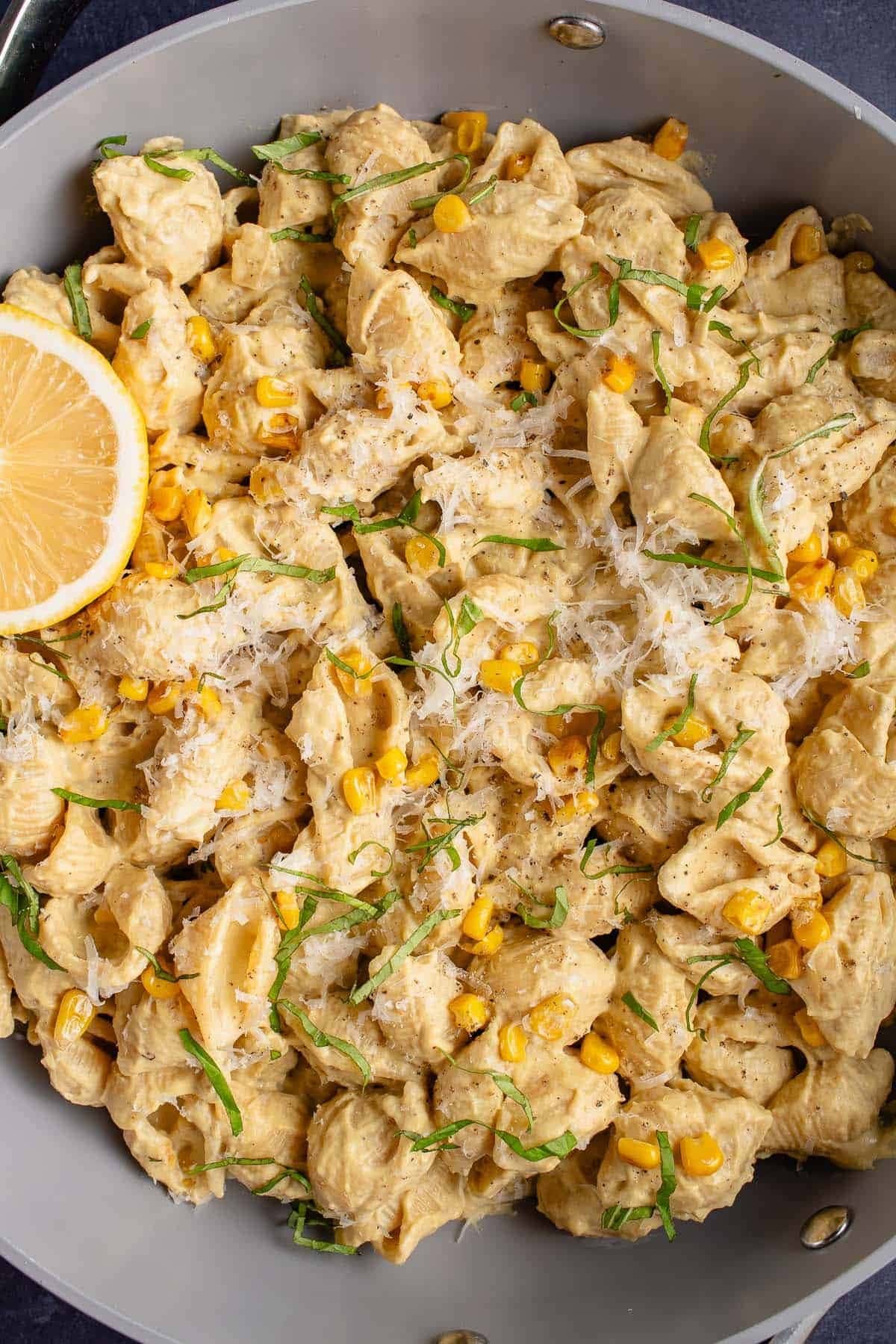 A serving of pasta with creamy sauce, corn kernels and cheese on a gray plate.