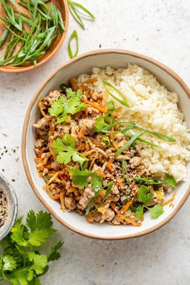 Egg roll served with white rice on a bowl garnished with cilantro leaves.