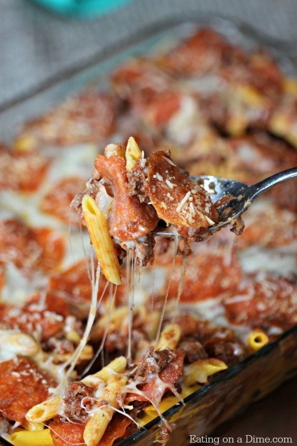 Spoon scooping cheesy pizza casserole form a glass dish.