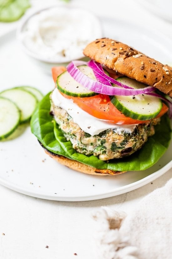 Burger with turkey patty full of garlic, olives, feta, spinach, and oregano with tomato, red onion and sliced cucumber.