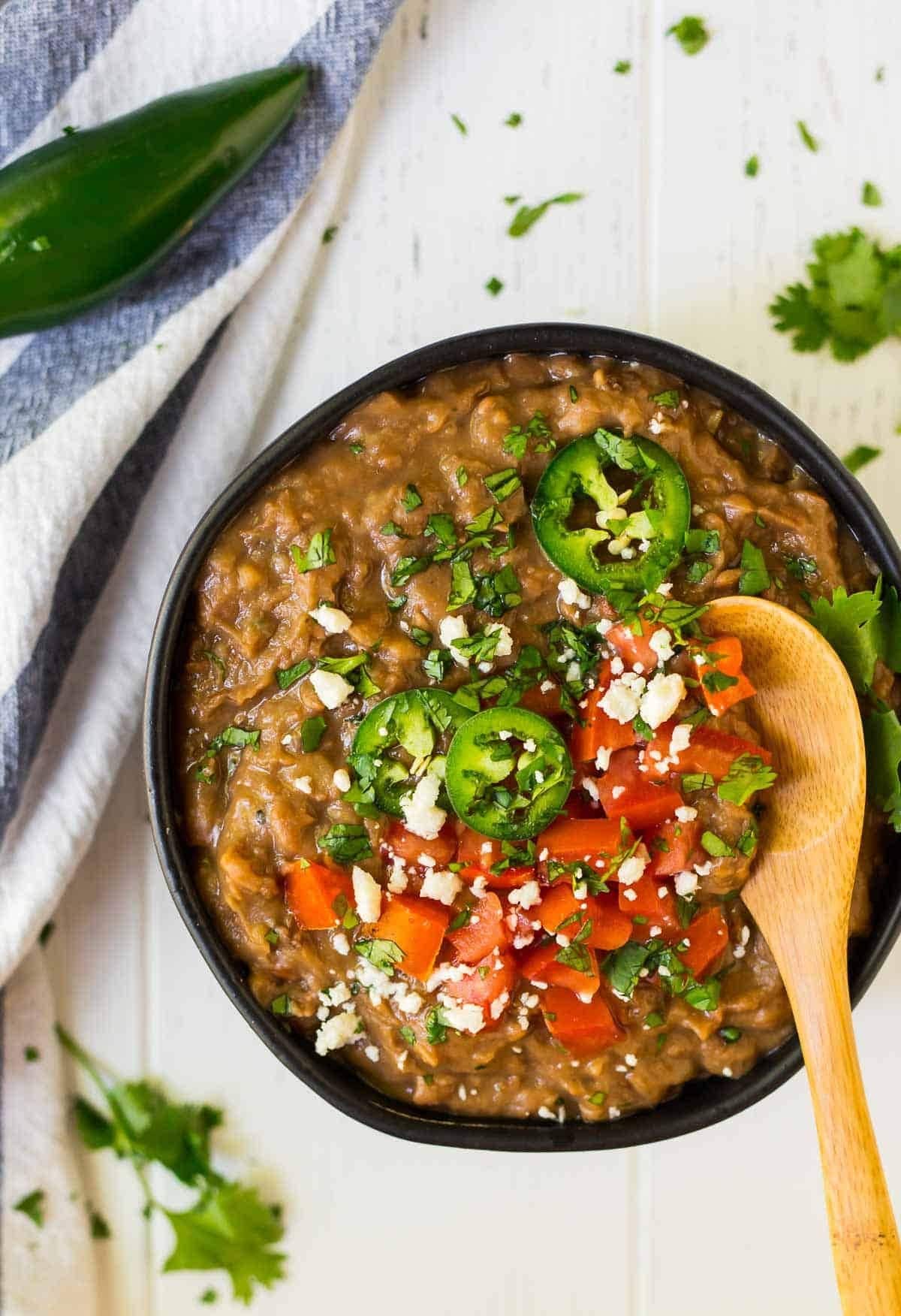 Bowl with refried beans garnished with chopped tomatoes, cheese, chopped parsley and pepper.