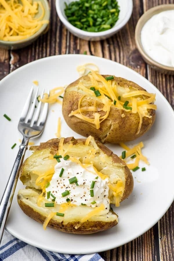 Baked potatoes with cream and grated cheese garnished with chopped onion leaves and pepper.