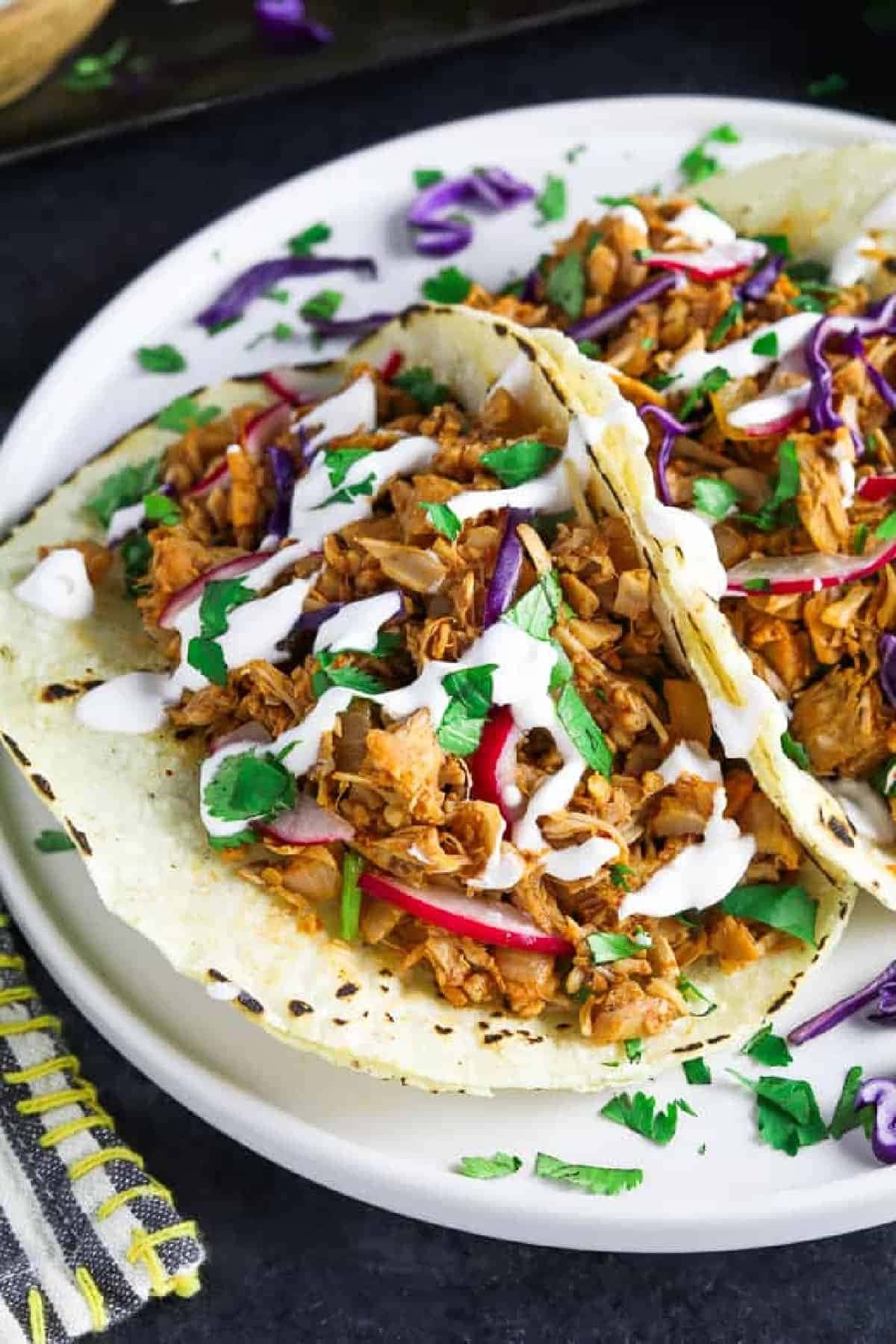 Taco with jackfruit and veggies filling topped with dressing.