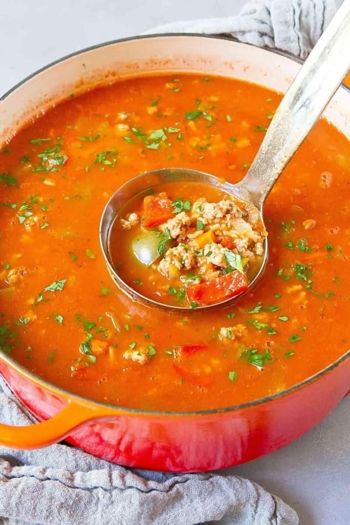 Stuffed pepper soup on a red pot scooped with a ladle.