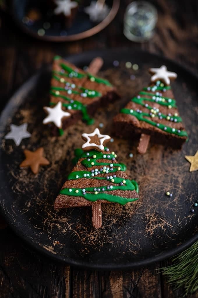 Triangle cut brownies decorated into Christmas tree with green icing and star candies.