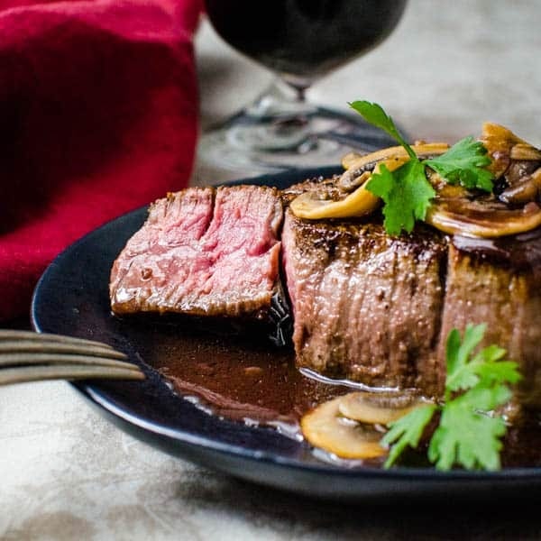 Sliced filet mignon bordelaise served on a black plate with sautéed mushroom garnish.