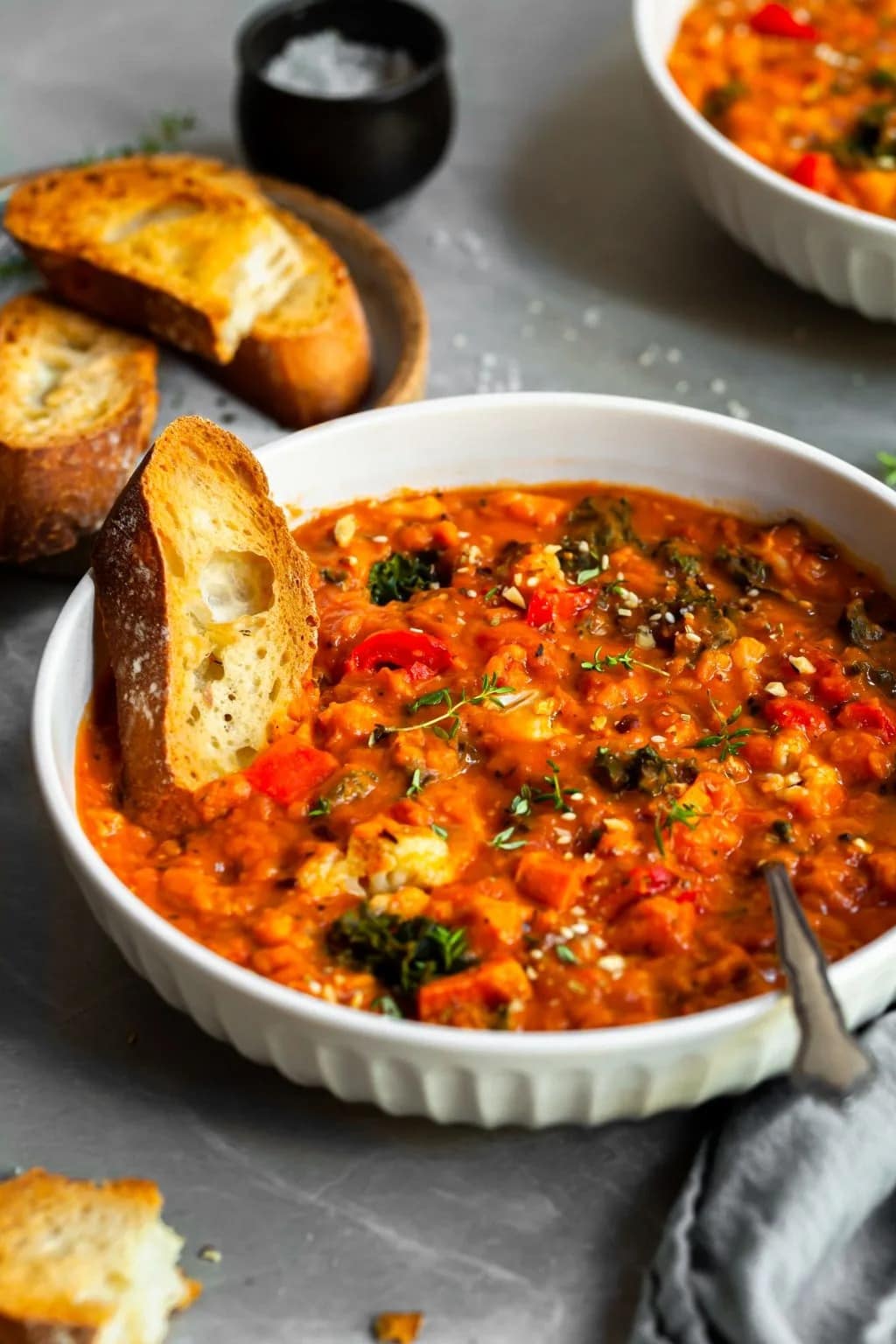 Toasted French bread dipped on a bowl of Roasted Vegetable and Red Lentil Stew